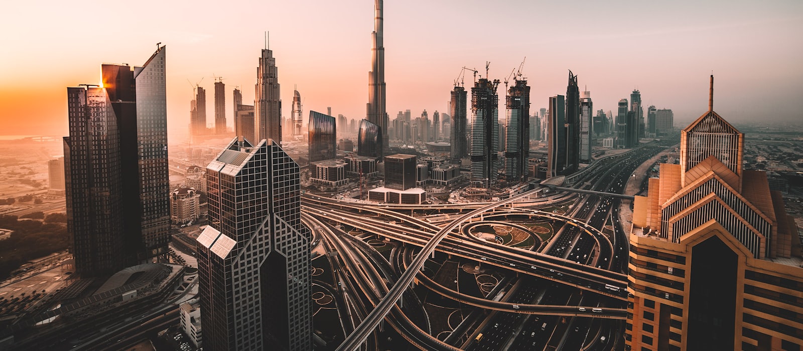The Dubai skyline at sunrise, with the Sheikh Zayed Road interchange below it.