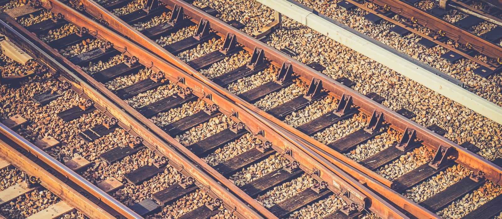 Railway points seen from above, where one rusted track divides into two across timber sleepers and gravel ballast.