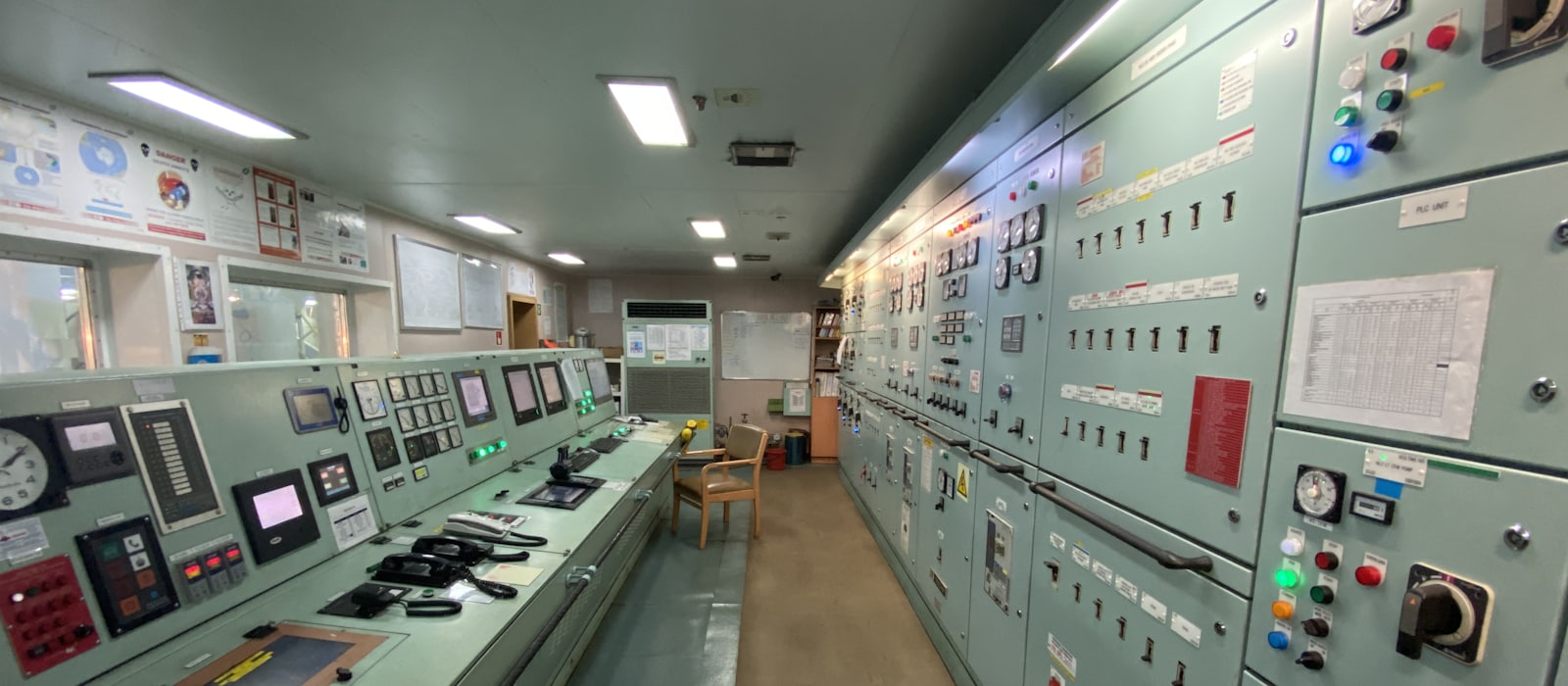 A ship's engine control room, banks of switches and gauges along both walls.