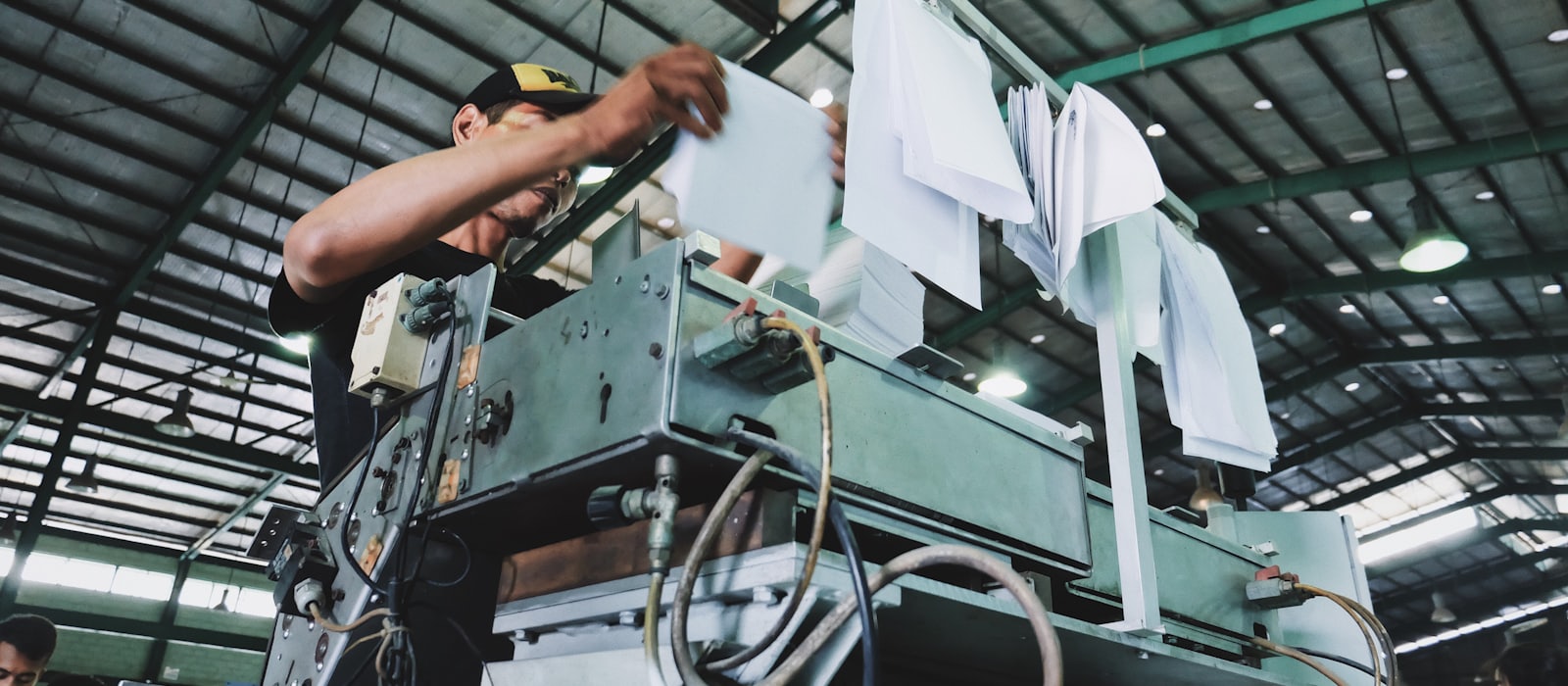 A worker feeding sheets into a large industrial press in a factory.