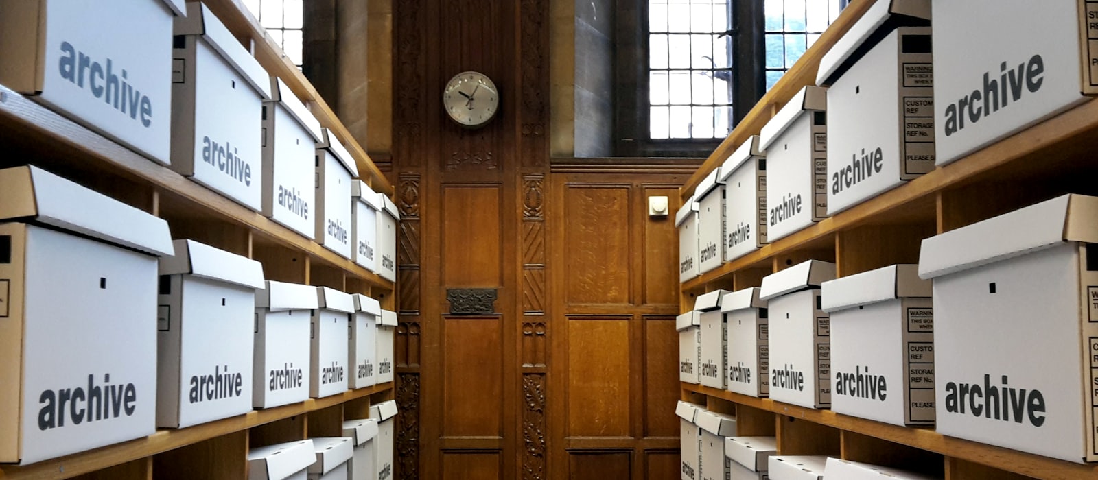 Rows of white archive boxes on wooden shelves in a panelled room.